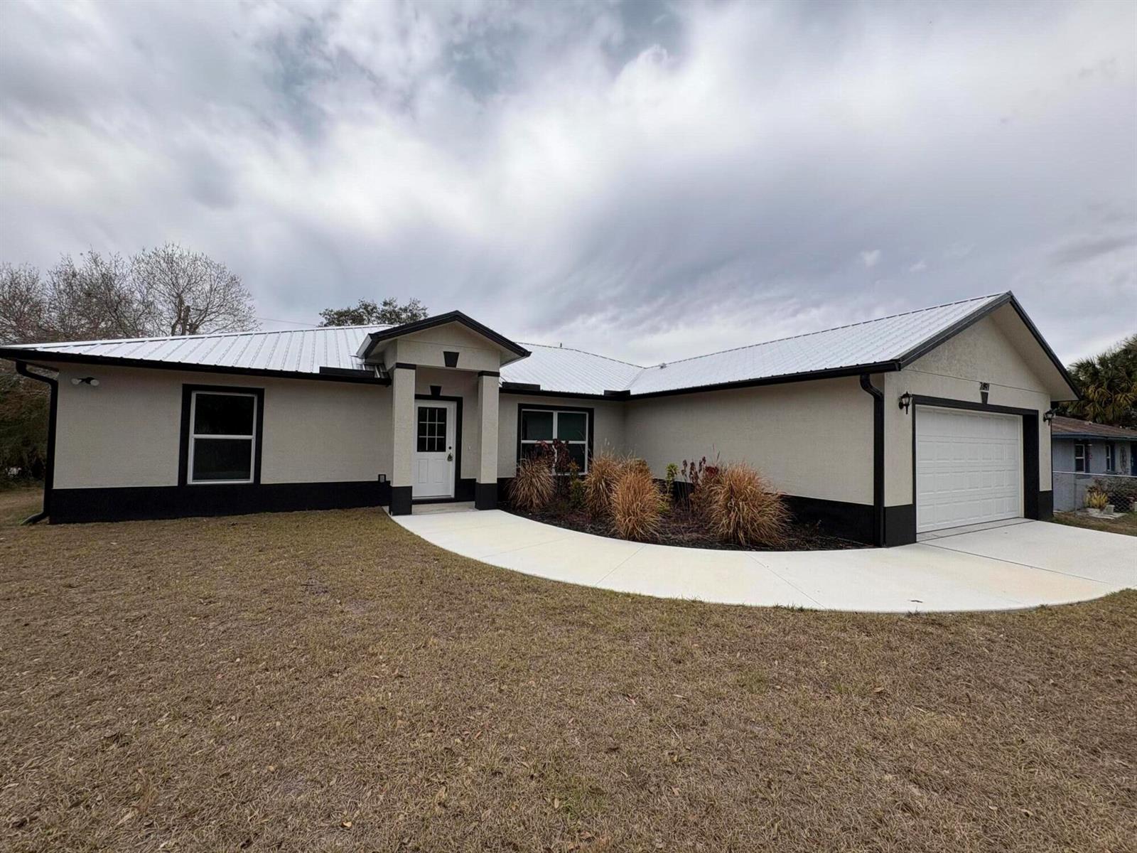 A single-story house with a white metal roof, beige stucco walls, and black trim — 2897 NW 37th Avenue, Okeechobee FL 34972, OKEECHOBEE, FL