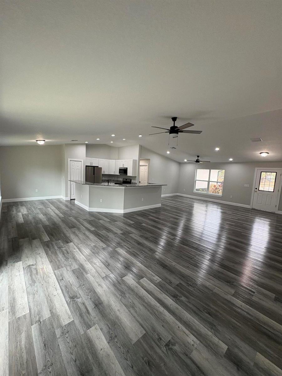 An open-concept living area features gray wood-look flooring, white kitchen cabinets, and a breakfast bar — 2897 NW 37th Avenue, Okeechobee FL 34972, OKEECHOBEE, FL