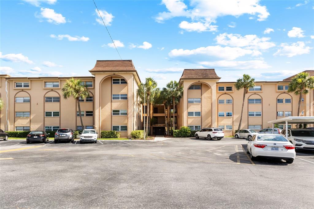 A multi-story apartment building with a parking lot in the foreground under a blue sky — 2525 W BAY DRIVE UNIT D13, LARGO, FL