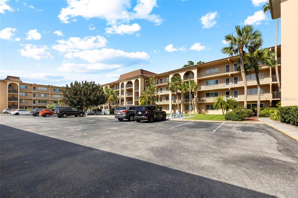 An exterior view of a multi-story apartment complex with a large parking lot in front — 2525 W BAY DRIVE UNIT D13, LARGO, FL