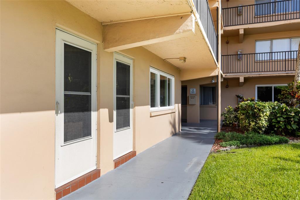 A ground-level apartment exterior features a covered walkway, two screen doors, and a window — 2525 W BAY DRIVE UNIT D13, LARGO, FL