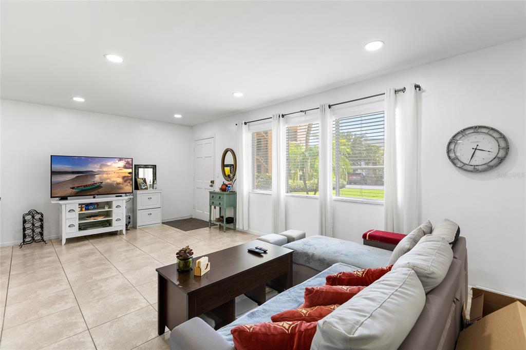 A living room features tile flooring, a sectional sofa, a television, and large windows — 2525 W BAY DRIVE UNIT D13, LARGO, FL