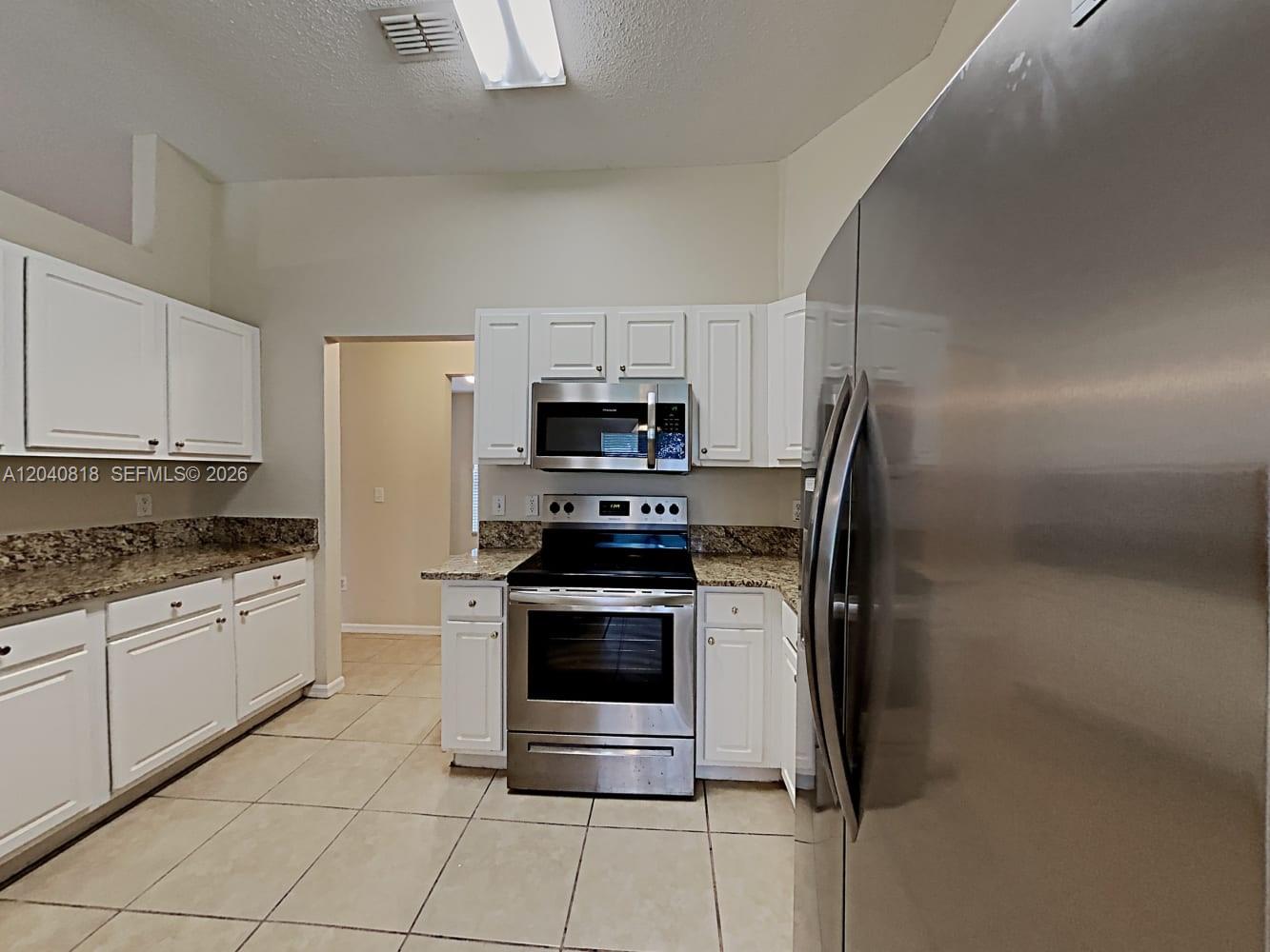 A kitchen features white cabinets, granite countertops, stainless steel appliances, and light tile flooring — PORT ST. LUCIE, FL
