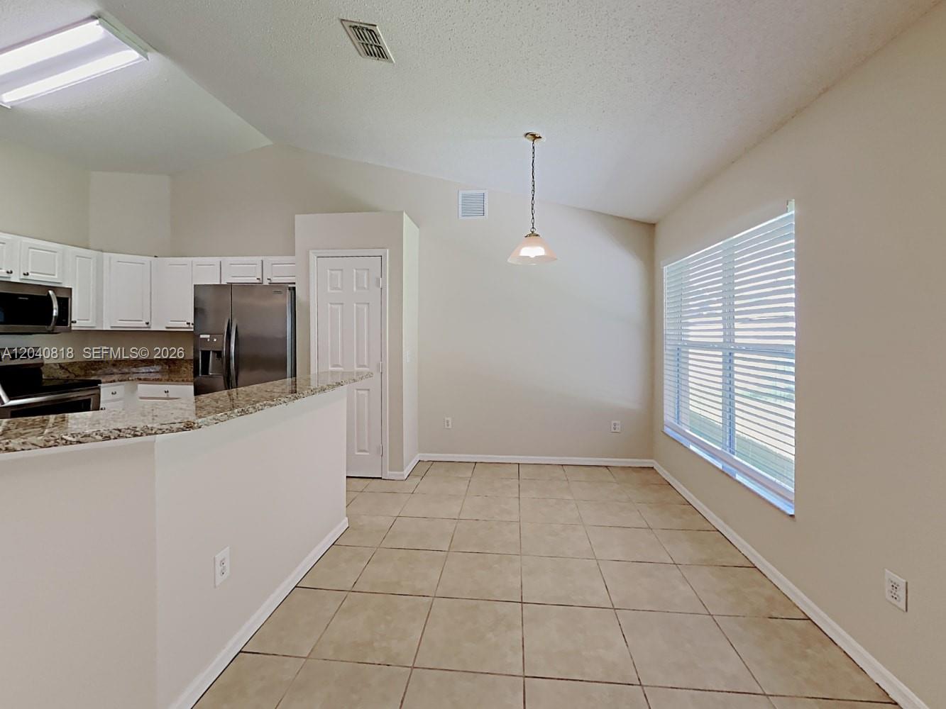 A kitchen with white cabinets and granite countertops opens into a tiled dining area — PORT ST. LUCIE, FL