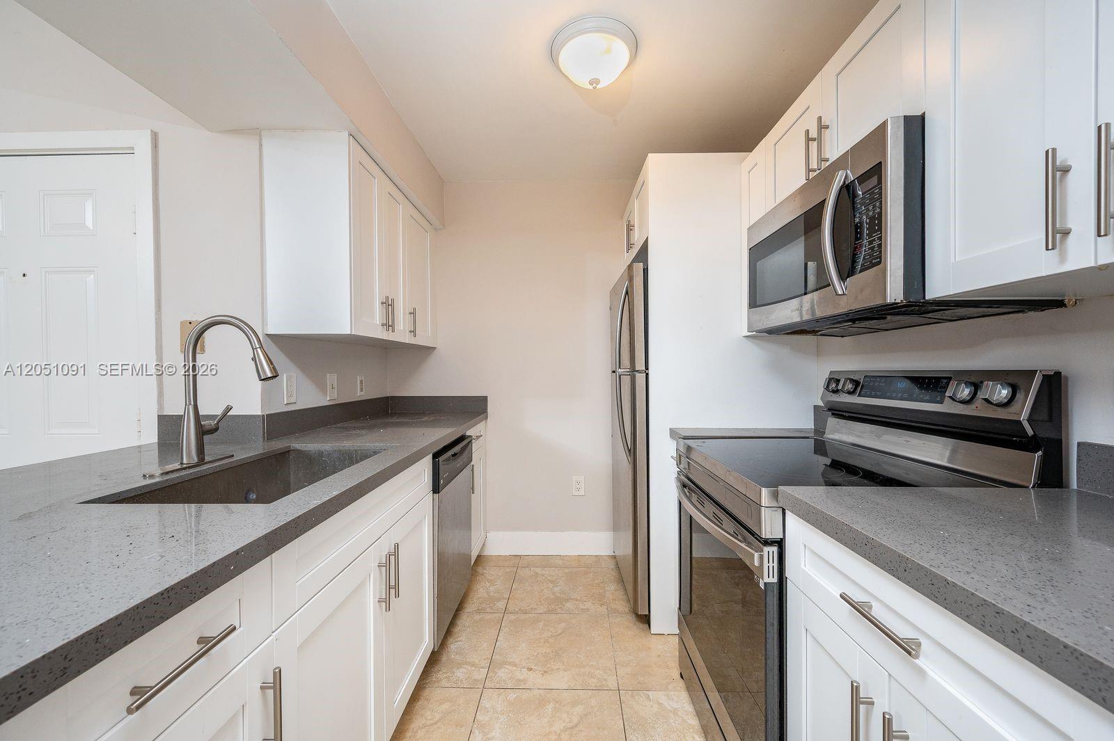 A galley kitchen features white cabinets, gray countertops, and stainless steel appliances — 15560 SW 104th Ter # 629, Miami FL 33196, MIAMI, FL