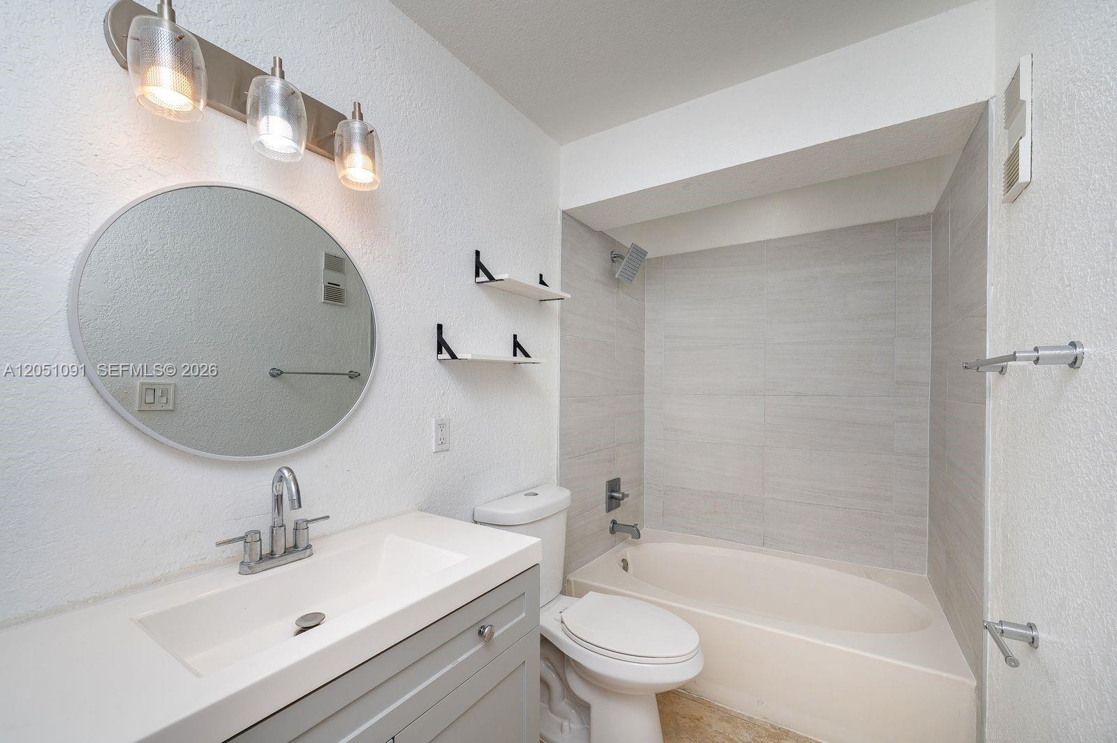 A bathroom features a gray vanity, a round mirror, a toilet, and a tiled bathtub — 15560 SW 104th Ter # 629, Miami FL 33196, MIAMI, FL