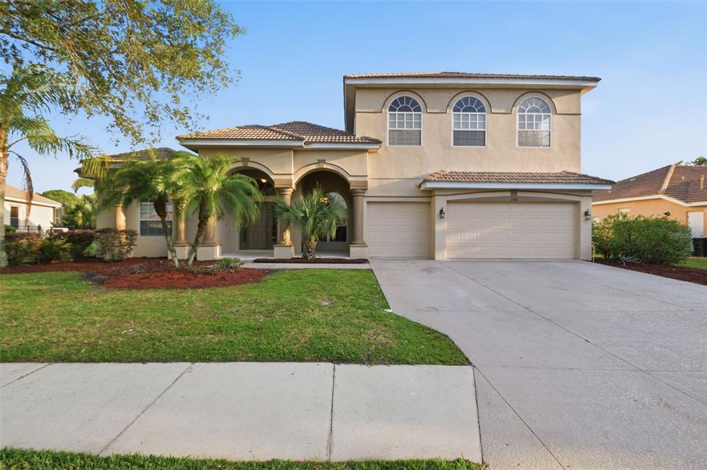 A two-story beige stucco house with a three-car garage and arched entryway — 12408 NATUREVIEW CIRCLE, BRADENTON, FL