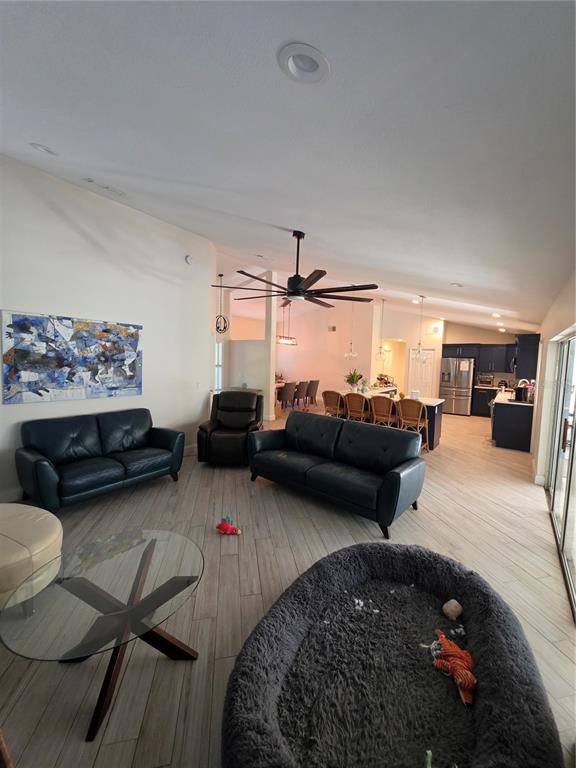 An open-concept living room features dark leather furniture, wood-look tile flooring, and a vaulted ceiling — 10158 BRANDON CIRCLE, ORLANDO, FL