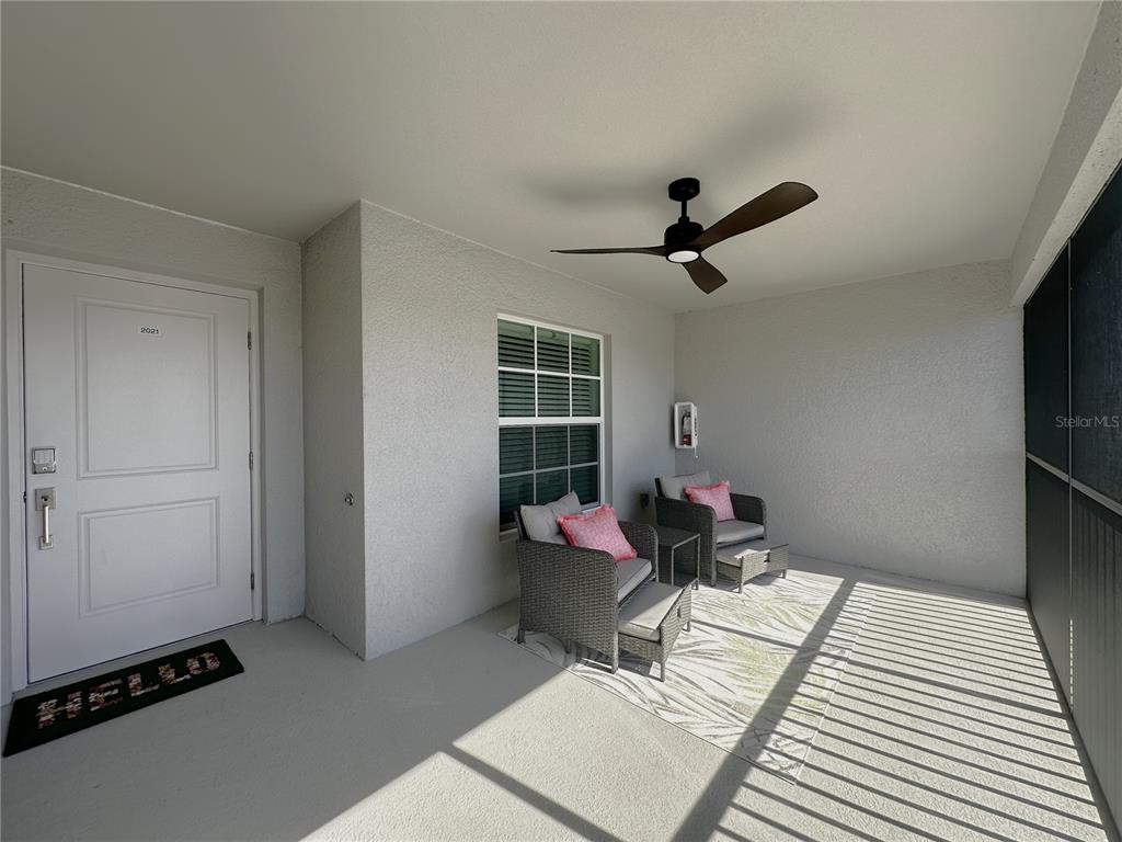 A covered patio features a ceiling fan, two wicker chairs with ottomans, and a white door — 14221 HERITAGE LANDING BOULEVARD UNIT 2021, PUNTA GORDA, FL