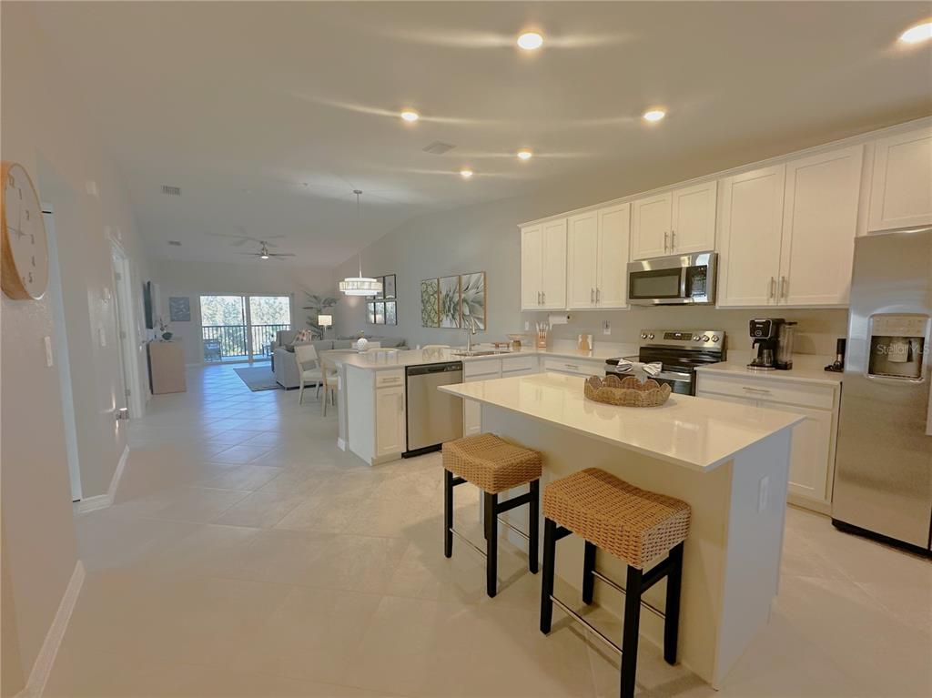 A bright, open-concept kitchen features white cabinetry, quartz countertops, and a central island with stools — 14221 HERITAGE LANDING BOULEVARD UNIT 2021, PUNTA GORDA, FL