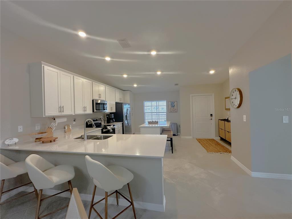 A modern kitchen features white cabinets, quartz countertops, a breakfast bar, and recessed lighting — 14221 HERITAGE LANDING BOULEVARD UNIT 2021, PUNTA GORDA, FL