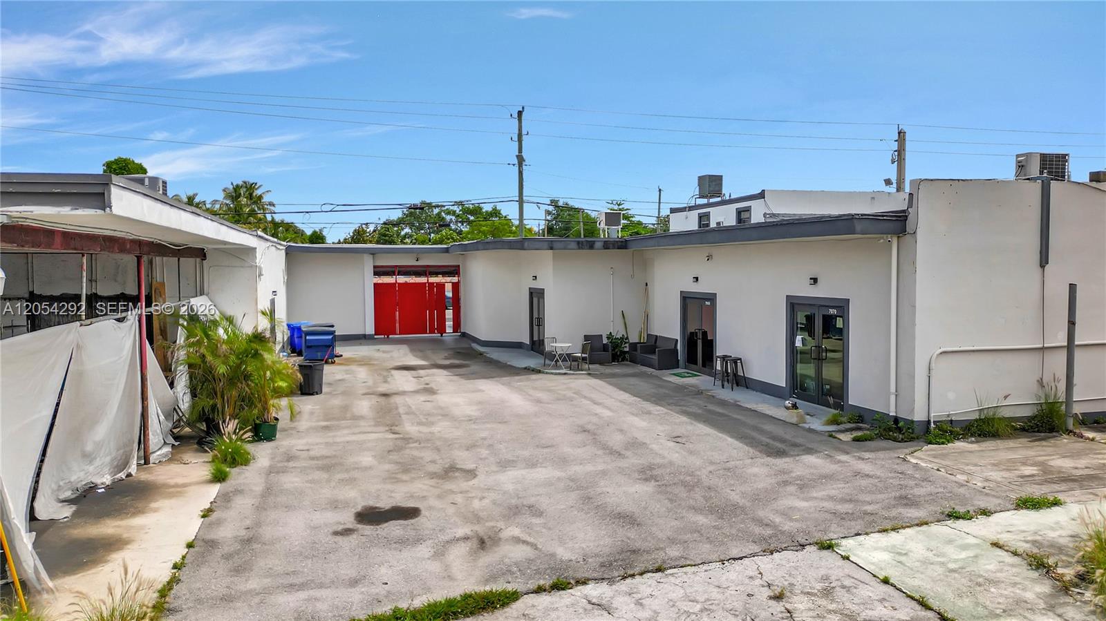 An exterior view shows a paved courtyard between two white commercial buildings with a red gate — 7000 NW 2 Ave # 7060, Miami FL 33150, MIAMI, FL