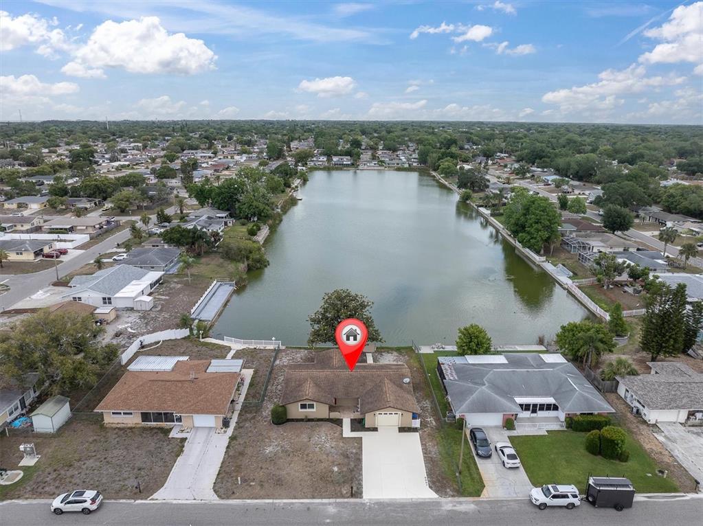 An aerial view shows a single-story house with a lakefront backyard and a concrete driveway — 8007 MIMOSA DRIVE, PORT RICHEY, FL