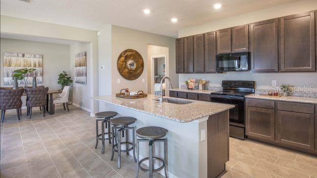 A kitchen features dark wood cabinets, granite countertops, a center island with stools, and tile flooring — 25125 THORNHILL DRIVE, SORRENTO, FL