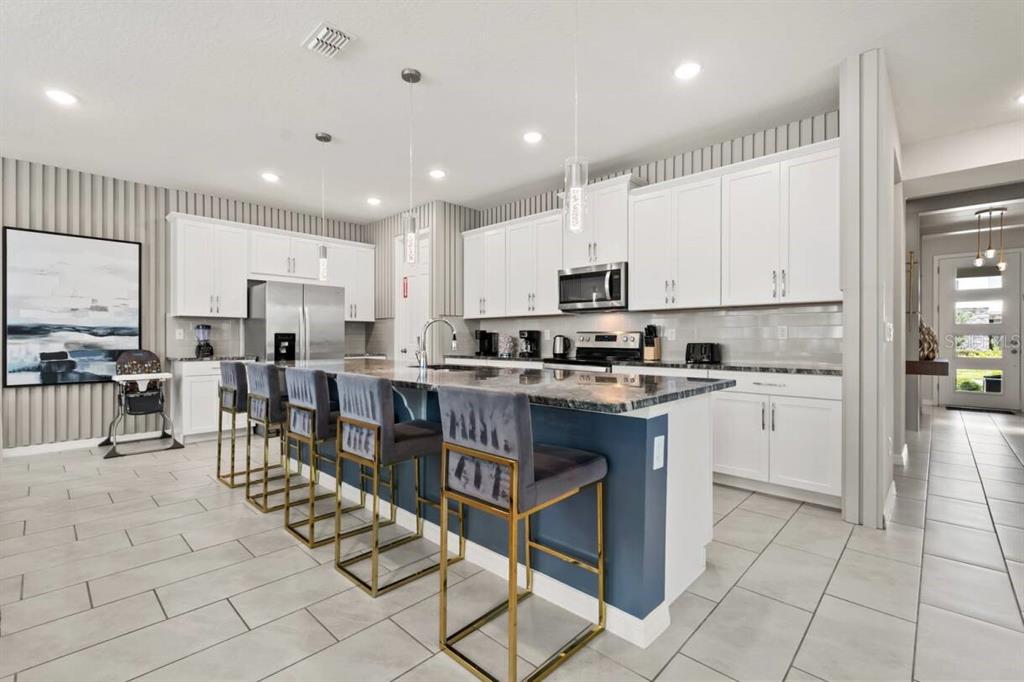 A modern kitchen features white cabinets, a blue island with bar stools, and tiled flooring — 1582 MERMAID COVE WAY, KISSIMMEE, FL