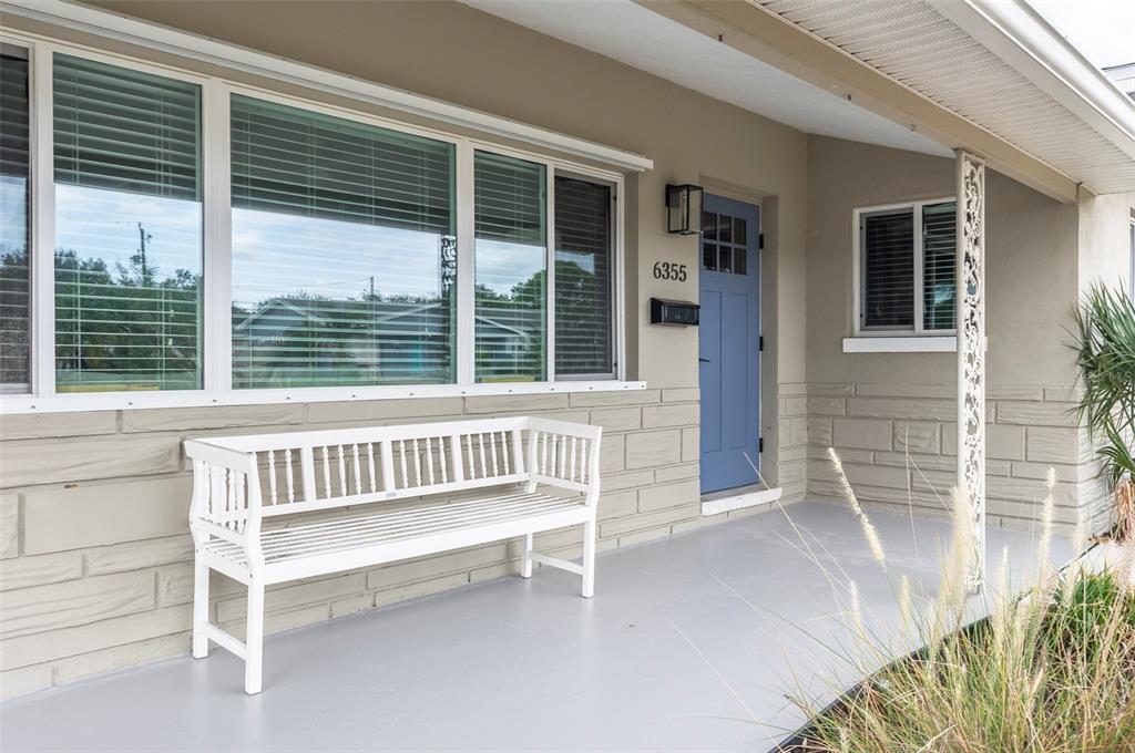 A white bench sits on a covered porch in front of a house with stone siding — 6355 23RD AVENUE N, ST PETERSBURG, FL