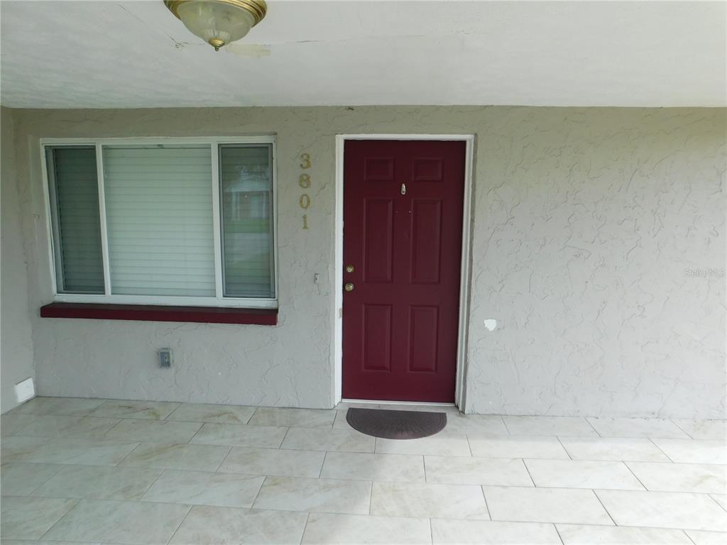 A red front door and a large window are on the stucco exterior of a house — 3801 DARLINGTON ROAD, HOLIDAY, FL