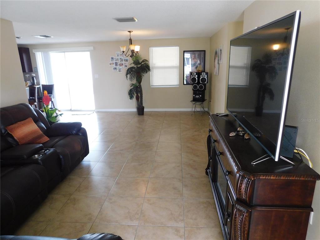 A living room features tile flooring, a dark leather sofa, and a television on a console — 3801 DARLINGTON ROAD, HOLIDAY, FL