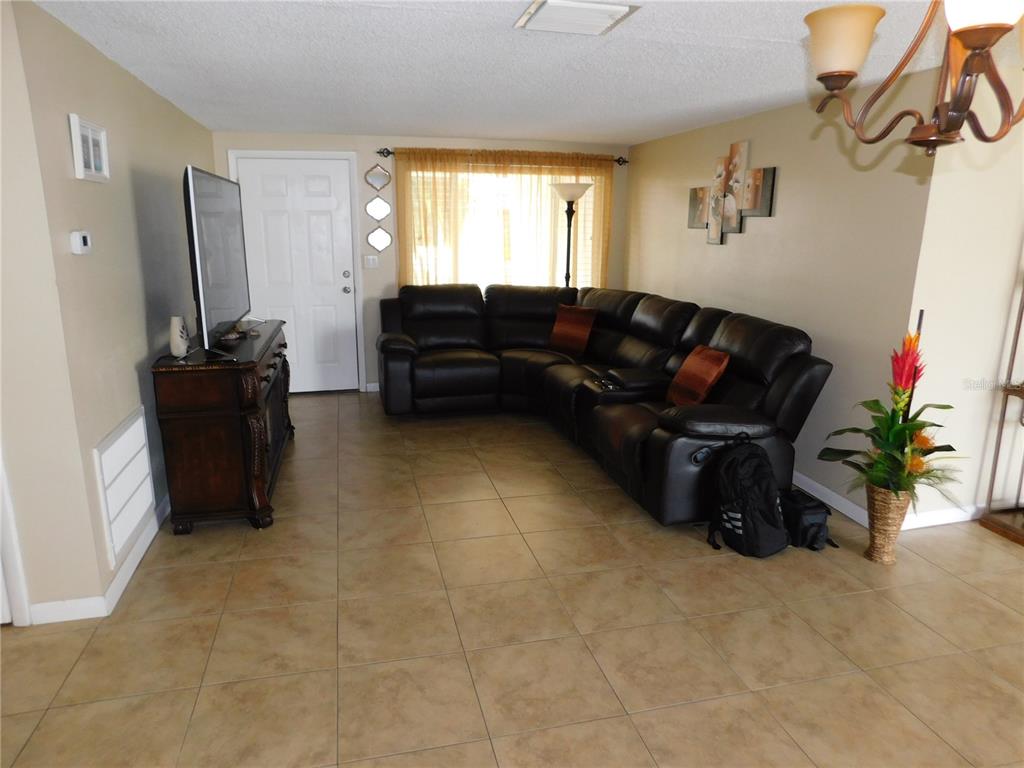 A living room features tan tile flooring, a dark leather sectional sofa, and a television console — 3801 DARLINGTON ROAD, HOLIDAY, FL