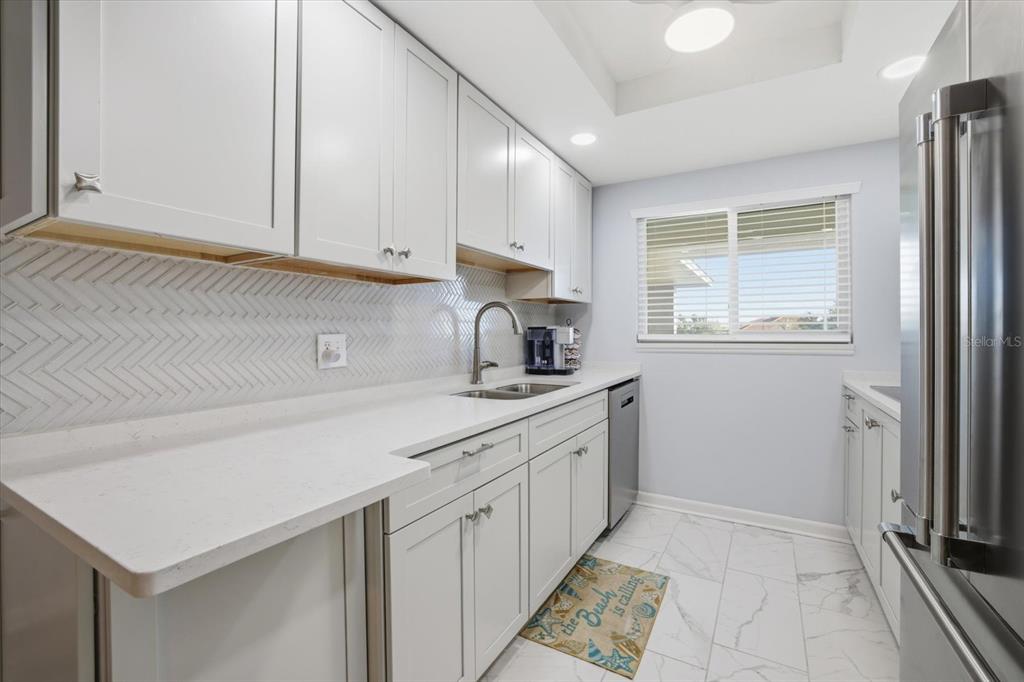 A bright kitchen features white shaker cabinets, white countertops, a herringbone backsplash, and marble-look flooring — 649 TAMIAMI TRAIL S UNIT 306, VENICE, FL