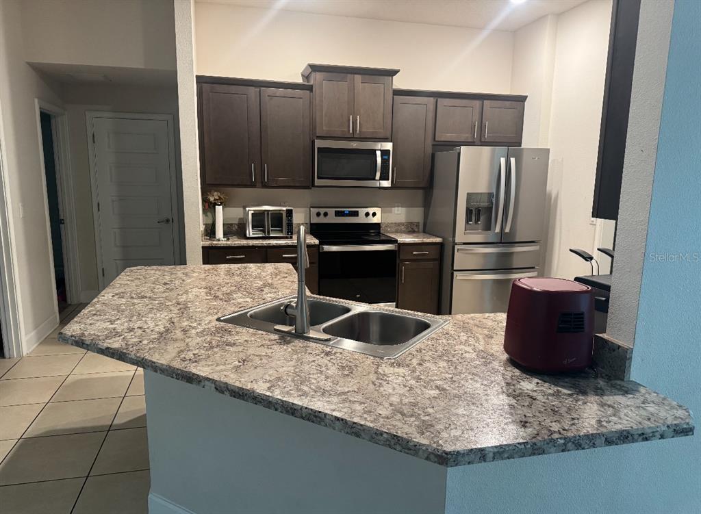 A kitchen features dark wood cabinets, stainless steel appliances, and a granite-topped island with sink — 333 ASHTON WOODS LANE, LEESBURG, FL