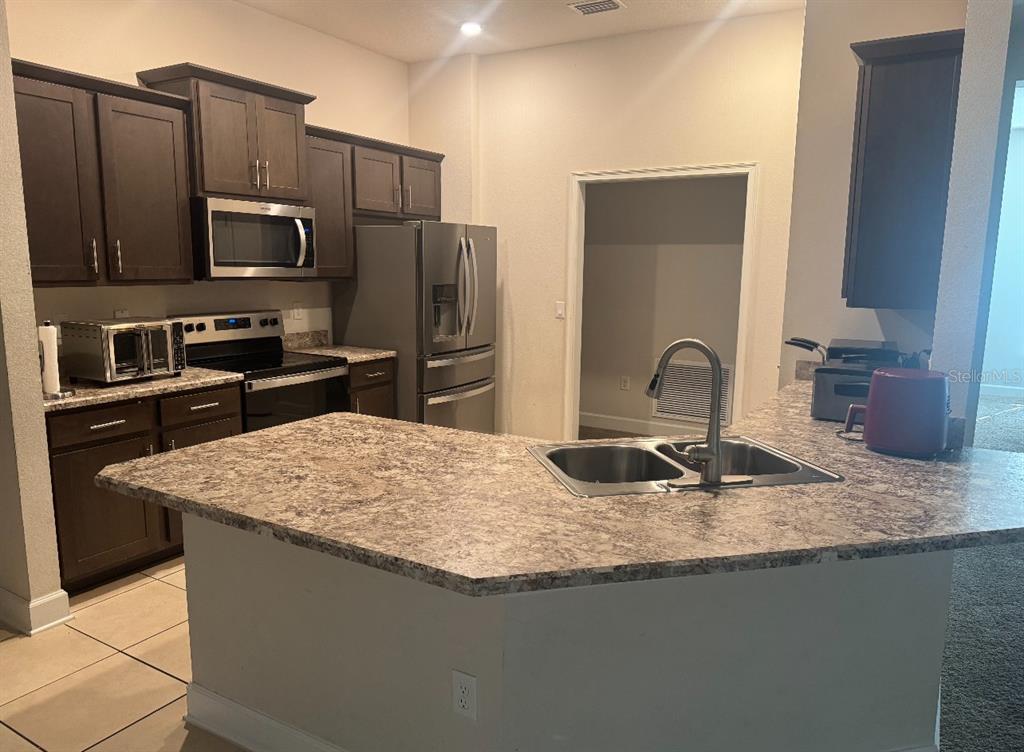 A kitchen features dark wood cabinets, stainless steel appliances, and a granite-look countertop island — 333 ASHTON WOODS LANE, LEESBURG, FL