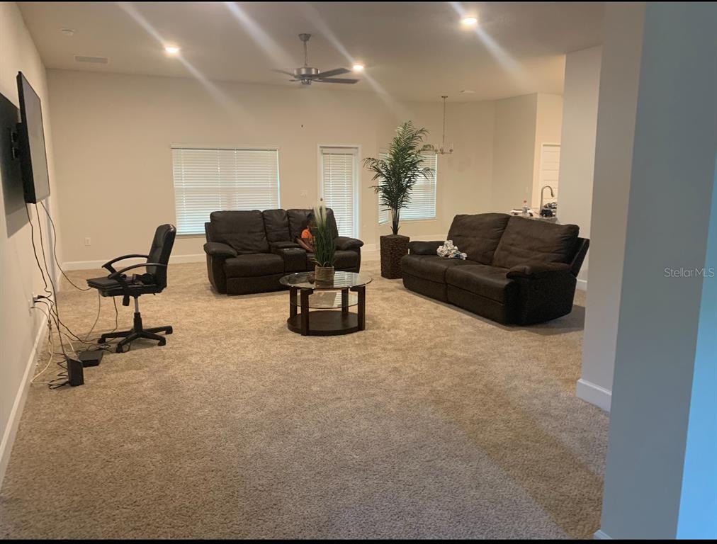 A living room features beige carpeting, two dark leather sofas, a glass coffee table, and a desk — 333 ASHTON WOODS LANE, LEESBURG, FL