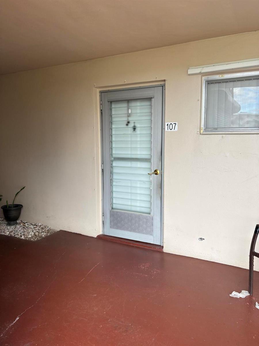 A gray screen door with the number 107 leads into a unit with a covered patio — 2606 Garden Drive S # 107, FL 33461, FL