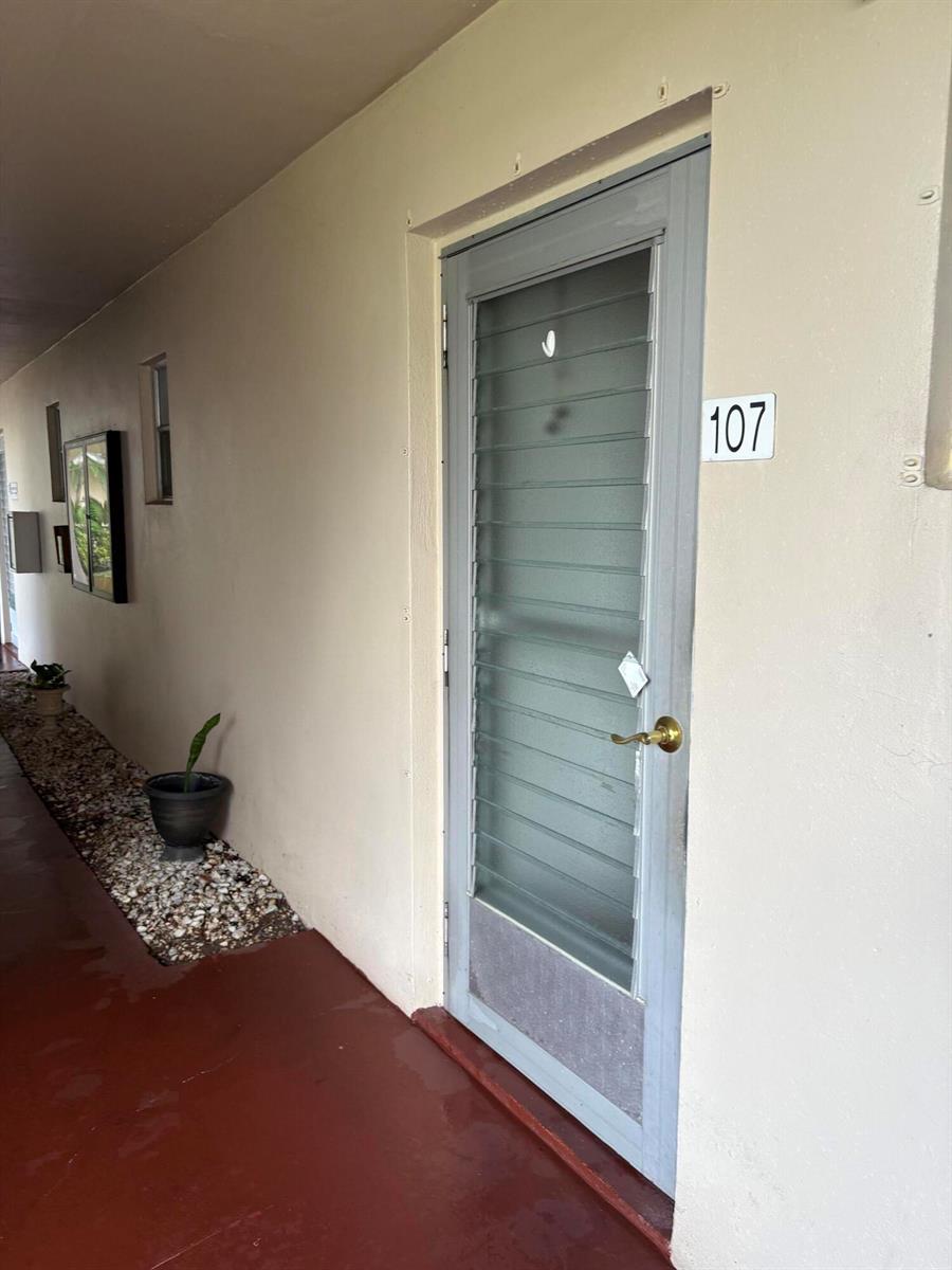 A gray louvered door labeled 107 sits along an outdoor walkway with a gravel planter — 2606 Garden Drive S # 107, FL 33461, FL
