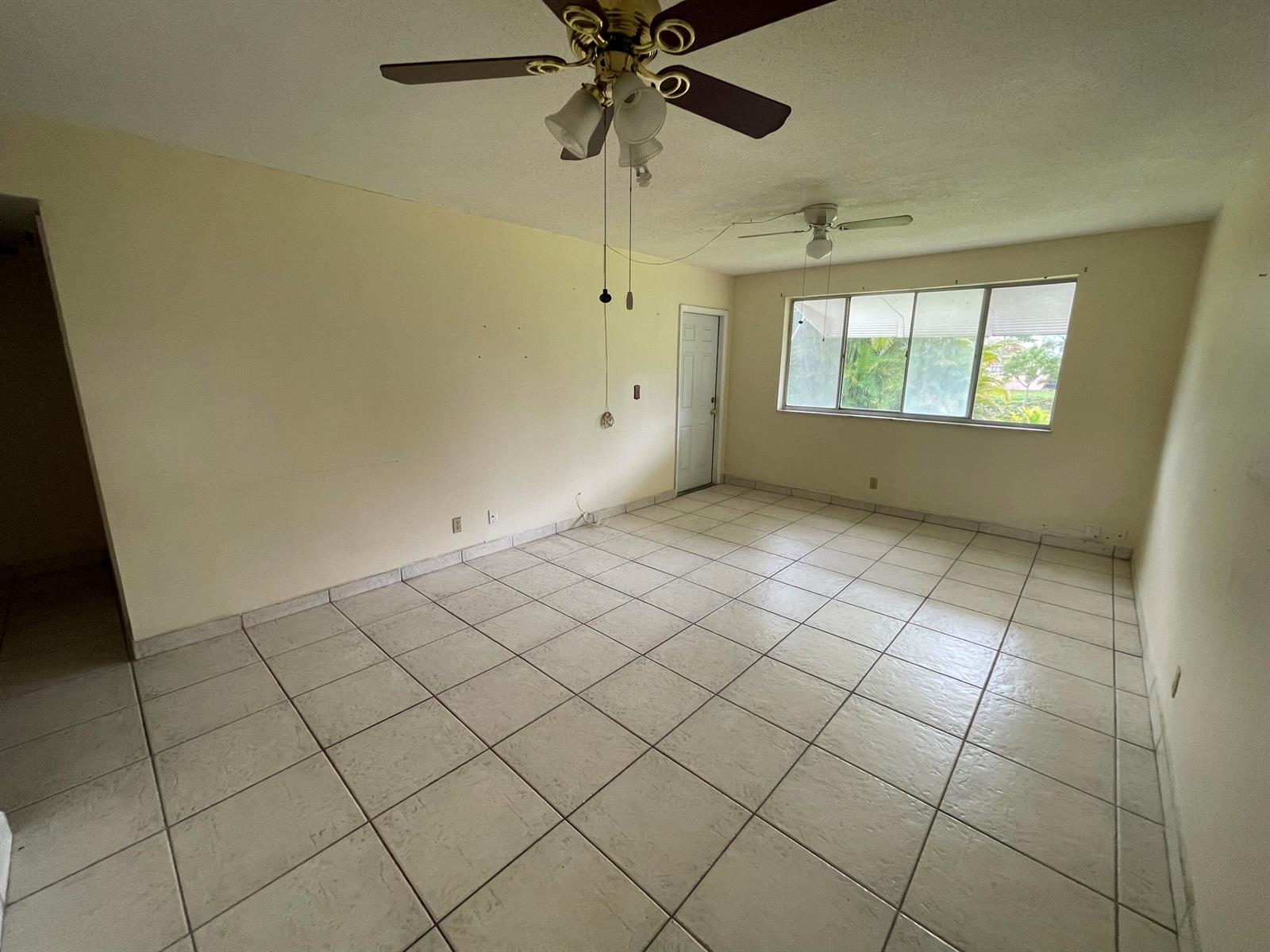 An empty room features light-colored tile flooring, two ceiling fans, and a large window — 2606 Garden Drive S # 107, FL 33461, FL