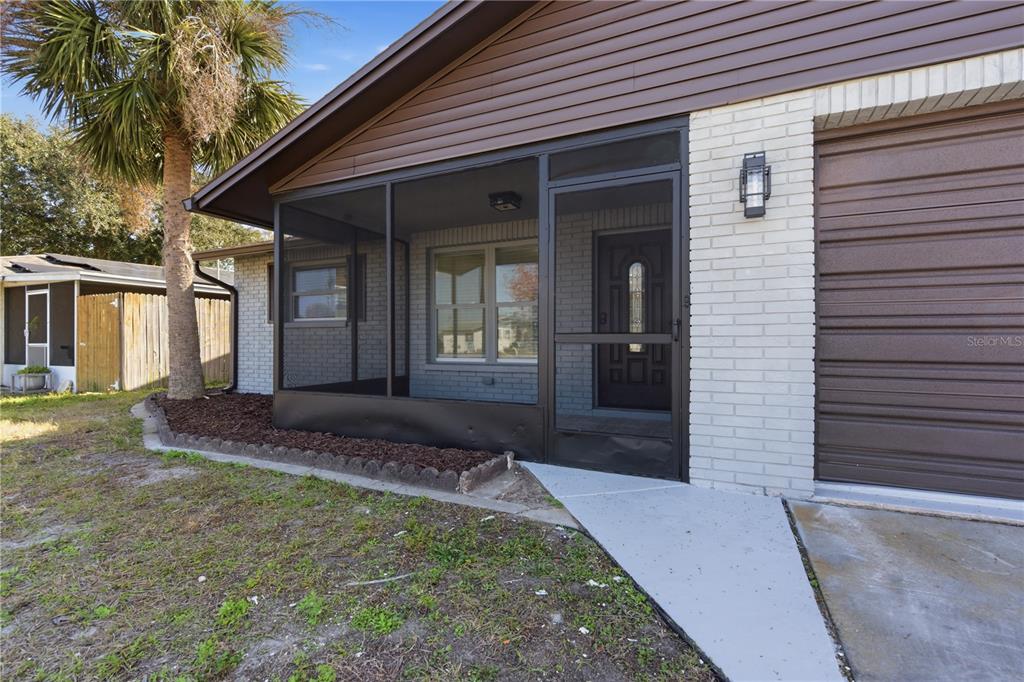 A screened-in front porch sits beside a garage on a house with brick siding — 5330 POINSETTIA DR, NEW PORT RICHEY, FL