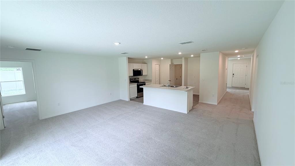 An open-concept living area features gray carpeting, a kitchen island, and white cabinetry — 234 BEECHWOOD LANE, PALM COAST, FL