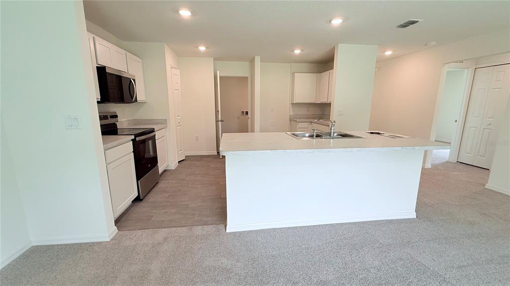 A kitchen with white cabinets, a central island, and stainless steel appliances overlooks a carpeted area — 234 BEECHWOOD LANE, PALM COAST, FL