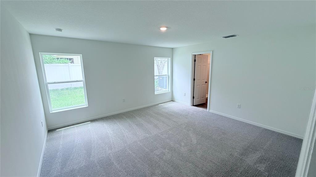 An empty bedroom features gray carpet, white walls, two windows, and an open doorway — 234 BEECHWOOD LANE, PALM COAST, FL