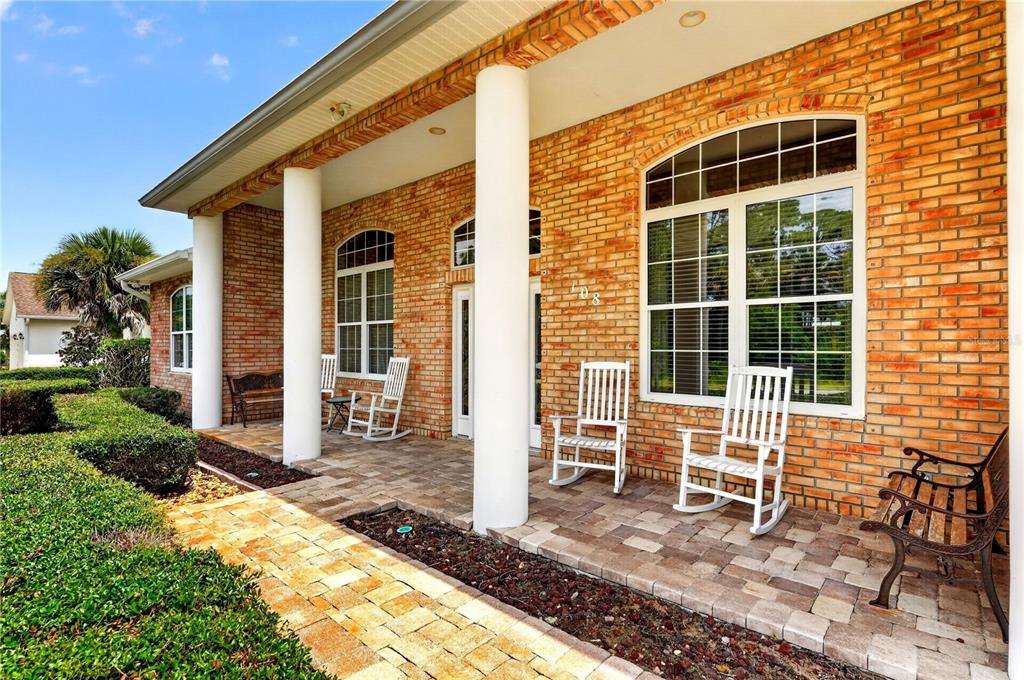 A brick house exterior features a covered porch with white columns and rocking chairs — 108 GODFREY ROAD, EDGEWATER, FL