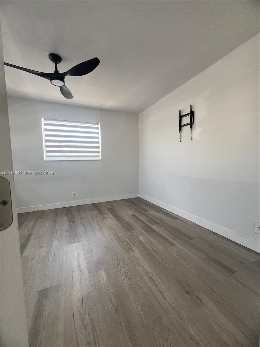 A bedroom features light wood-look flooring, white walls, a ceiling fan, and a wall-mounted TV bracket — 1711 Thomas St, Hollywood FL 33020, HOLLYWOOD, FL