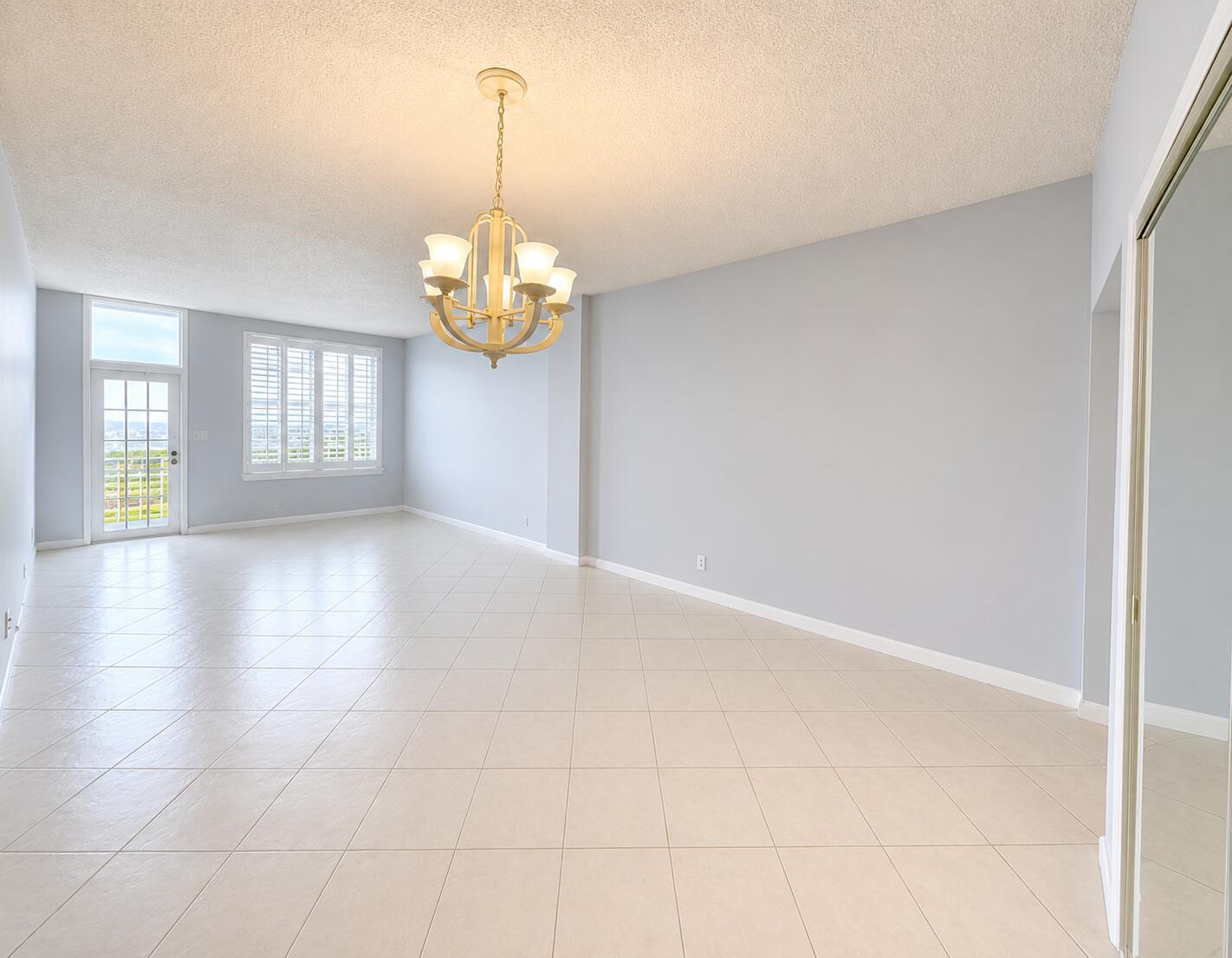 An empty room with light blue walls, beige tile flooring, and a traditional chandelier — 2851 S Ocean Boulevard # 7s, Boca Raton FL 33432, BOCA RATON, FL