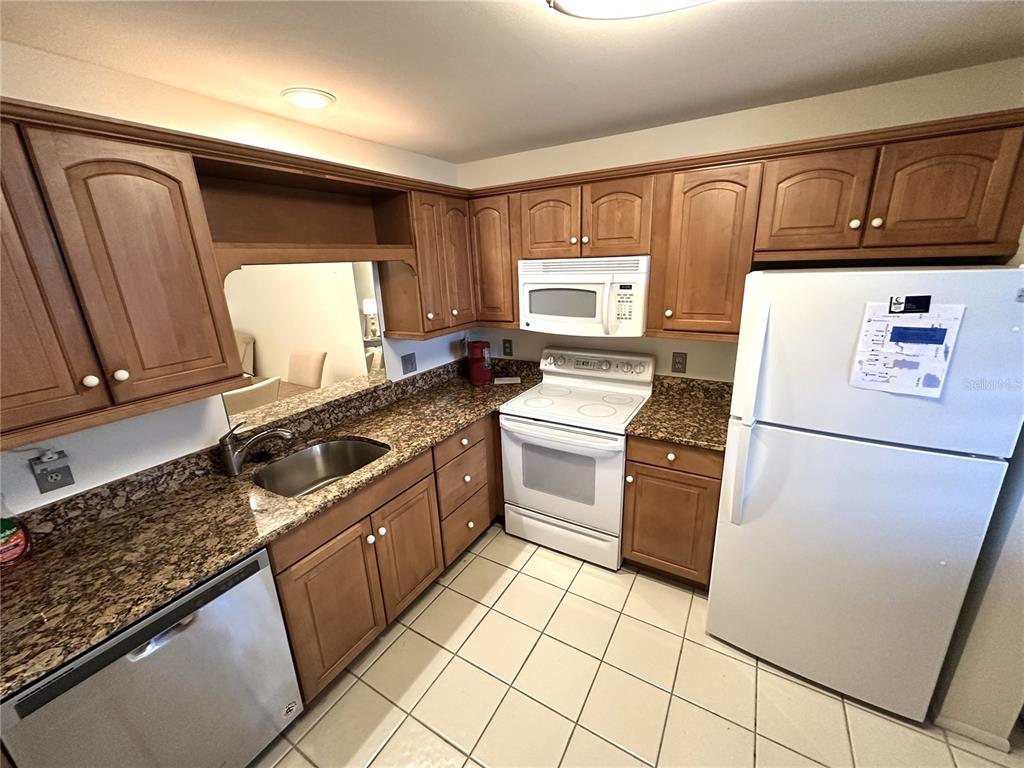 A kitchen features wood cabinets, granite countertops, white appliances, and light-colored tile flooring — 645 WOODLAWN DRIVE, BRADENTON, FL