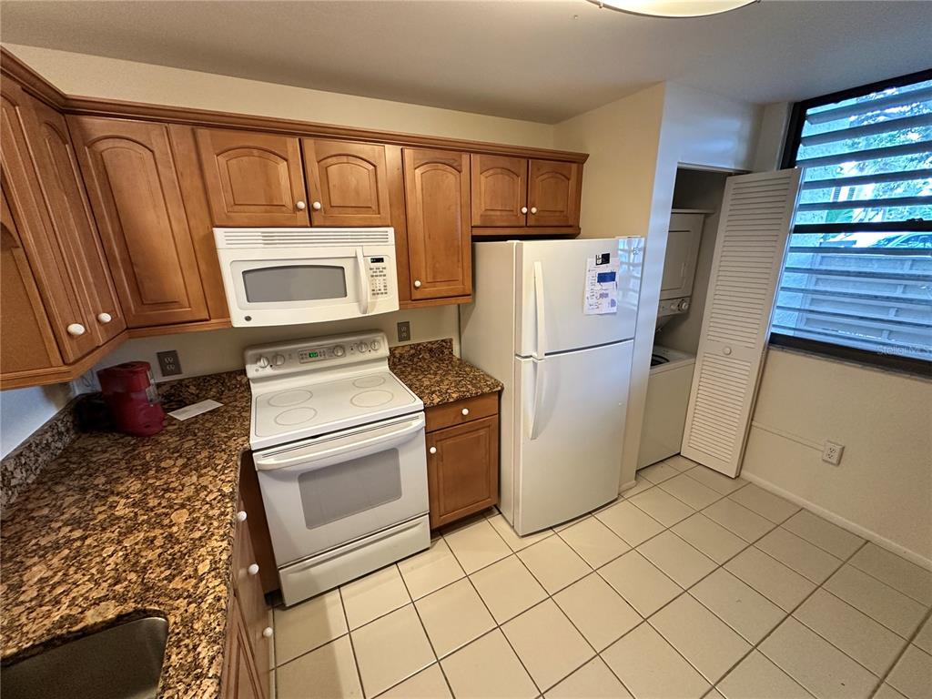 A kitchen features wood cabinets, granite countertops, white appliances, and tiled flooring — 645 WOODLAWN DRIVE, BRADENTON, FL