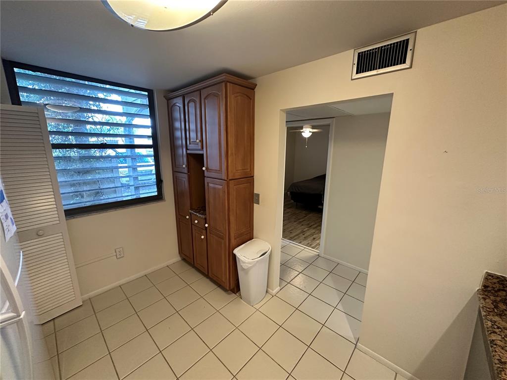 A kitchen area features light tile flooring, a tall wooden cabinet, and a doorway leading inside — 645 WOODLAWN DRIVE, BRADENTON, FL