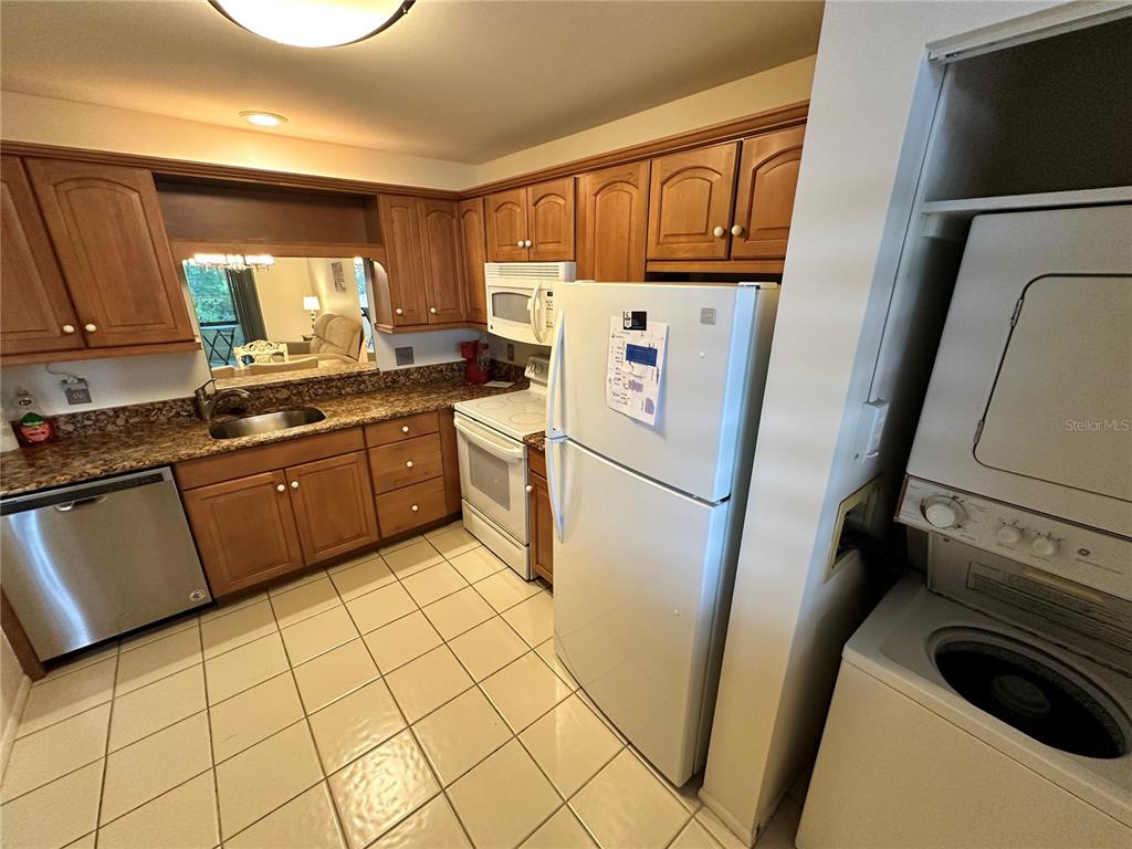 A kitchen features wood cabinets, granite countertops, stainless steel appliances, and an adjacent laundry area — 645 WOODLAWN DRIVE, BRADENTON, FL