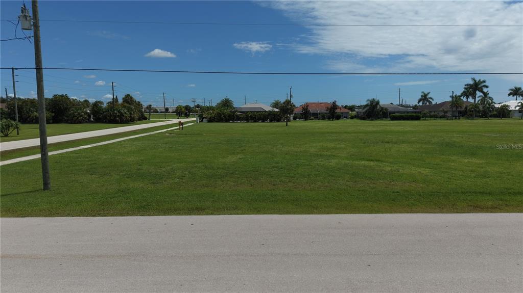 A wide, grassy vacant lot sits along a paved road under a blue sky — 7310 S BLUE SAGE, PUNTA GORDA, FL