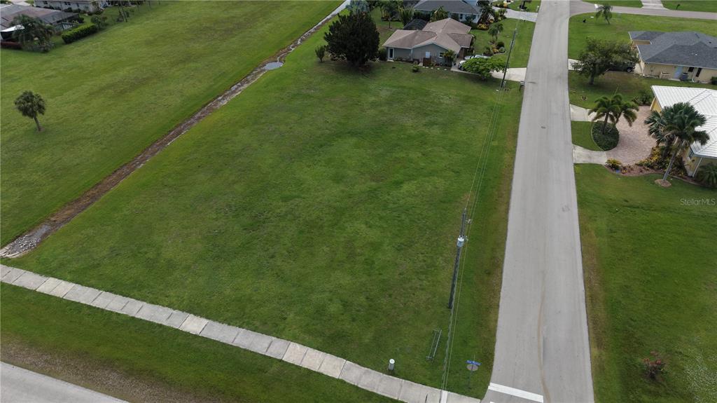 An aerial view shows a vacant, grassy residential lot bordered by a road and sidewalk — 7310 S BLUE SAGE, PUNTA GORDA, FL