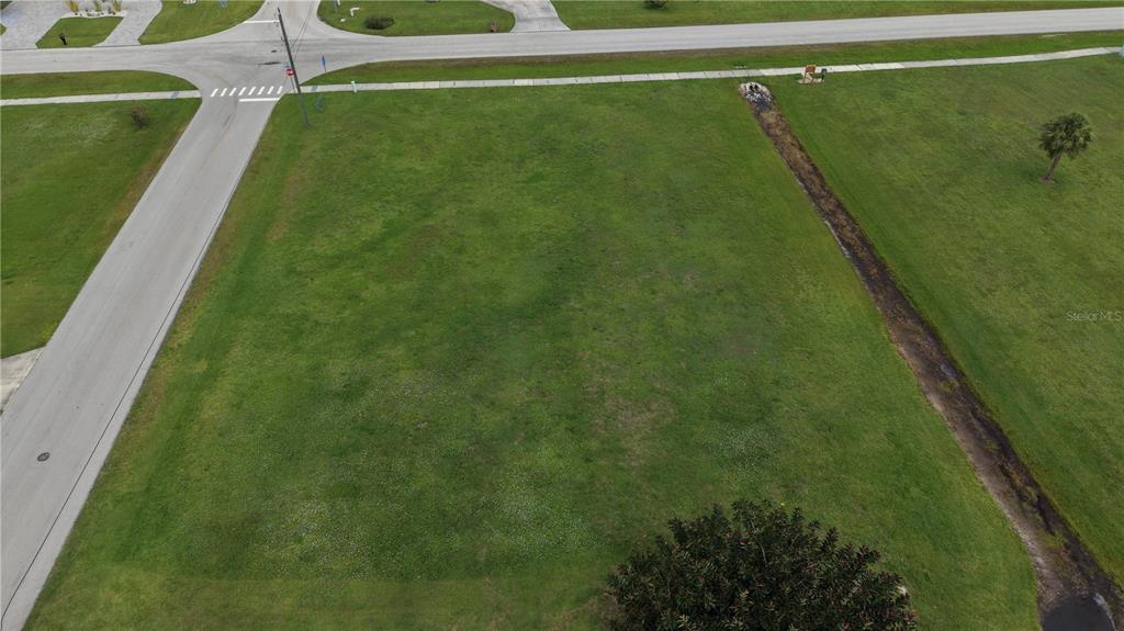 An aerial view shows a vacant, grassy residential lot bordered by paved roads — 7310 S BLUE SAGE, PUNTA GORDA, FL