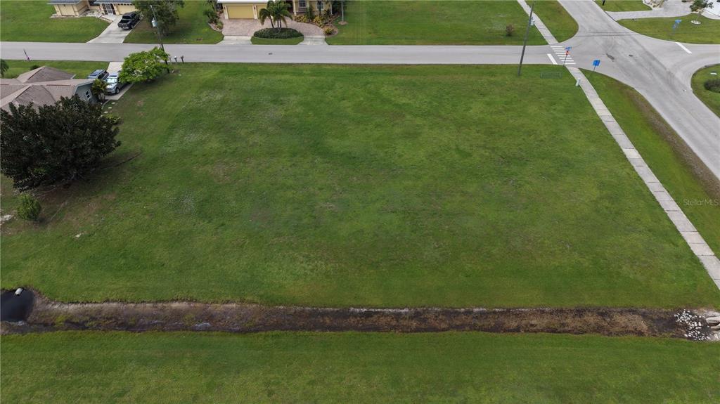 An aerial view shows a vacant, grassy residential lot situated on a corner street intersection — 7310 S BLUE SAGE, PUNTA GORDA, FL