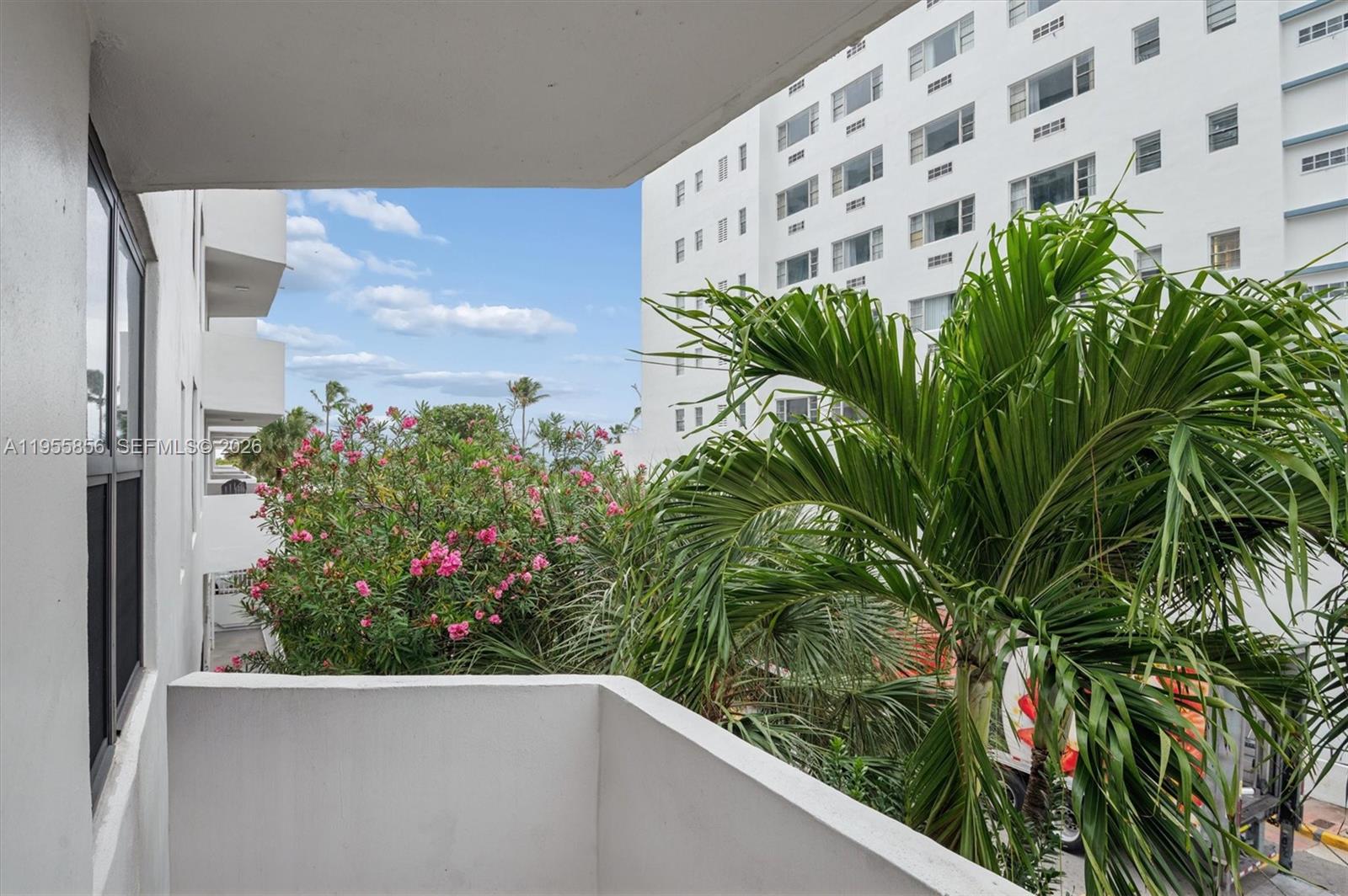 A view from a balcony overlooking a palm tree, flowering bushes, and a white building — 4301 Collins Ave # 202, Miami Beach FL 33140, MIAMI BEACH, FL