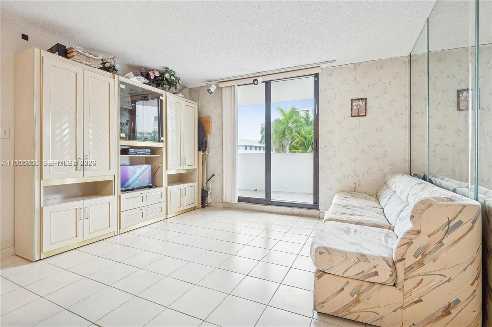 A living room features white tile floors, a large entertainment center, and a sliding glass door — 4301 Collins Ave # 202, Miami Beach FL 33140, MIAMI BEACH, FL