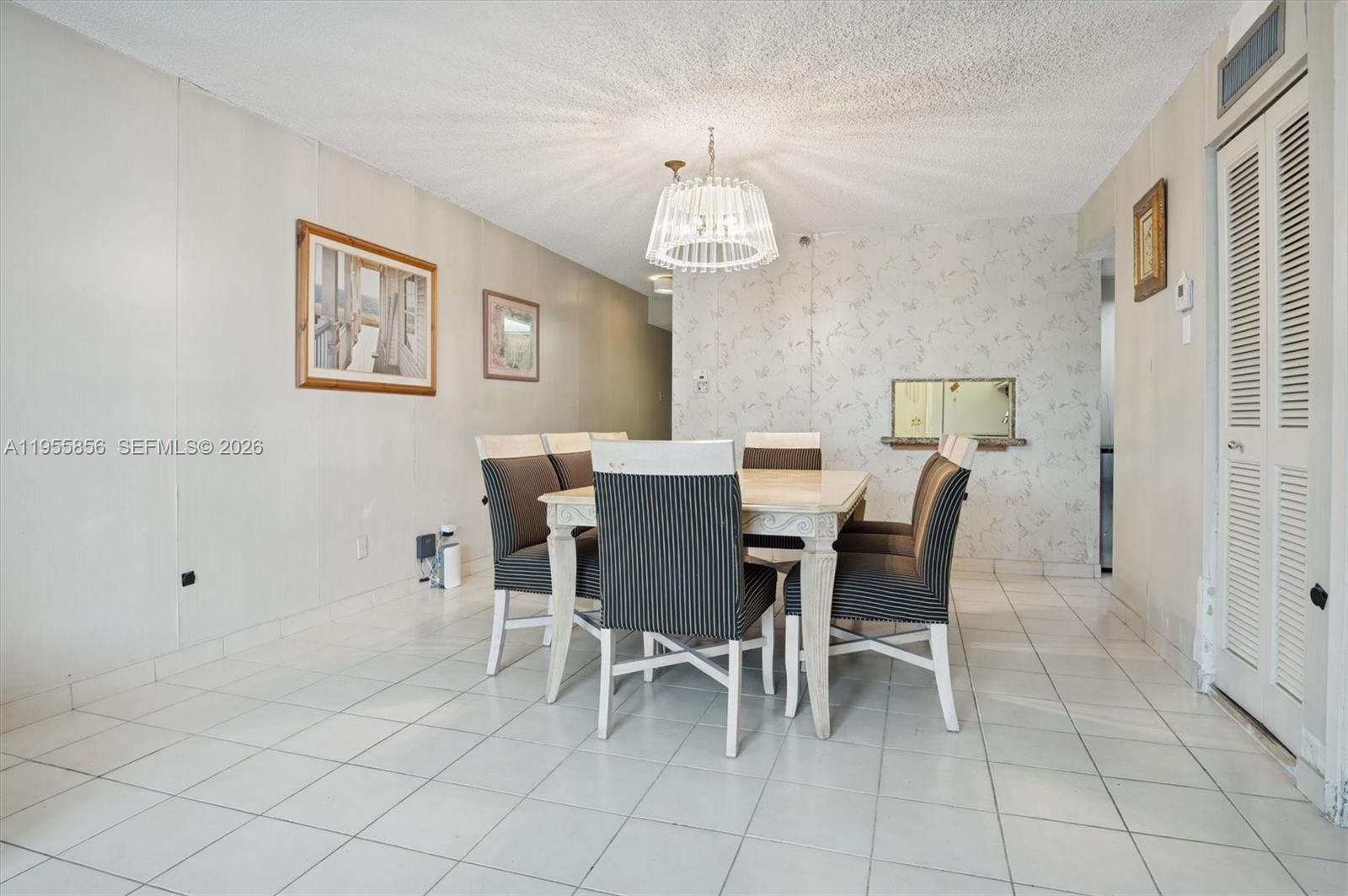A dining room features a white table with striped chairs, a chandelier, and tiled floors — 4301 Collins Ave # 202, Miami Beach FL 33140, MIAMI BEACH, FL