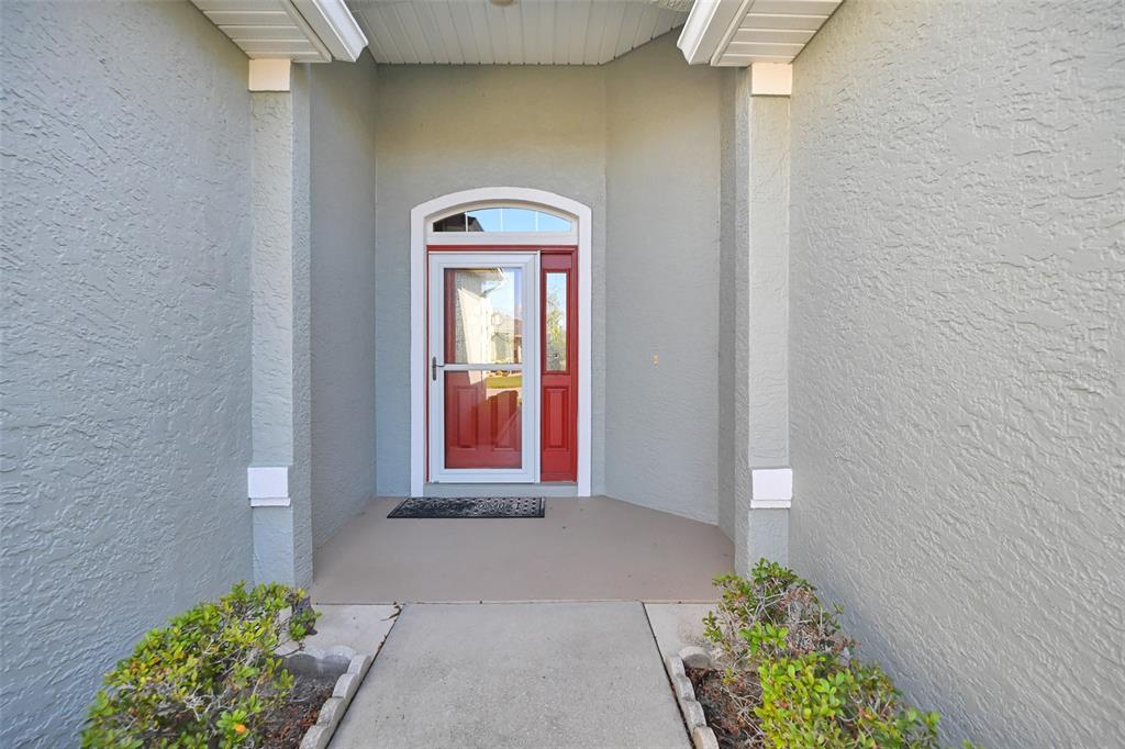 A red front door with a storm door is centered in a covered entryway — 7981 SW 81ST LOOP, OCALA, FL