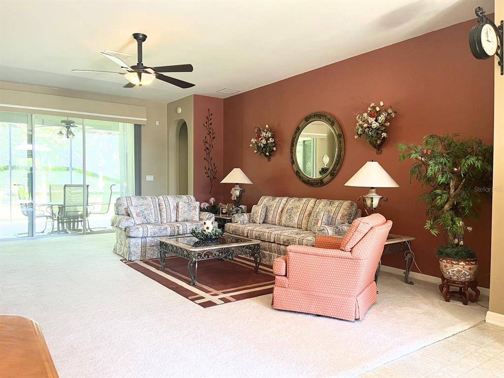 A living room features a rust-colored accent wall, floral sofas, and a sliding glass door — 7981 SW 81ST LOOP, OCALA, FL
